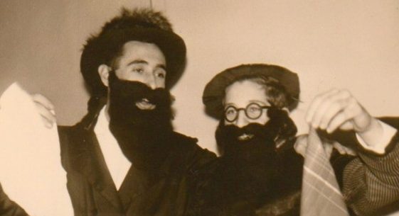 Photographie en noir et blanc montrant deux participants costumés lors d’une célébration de Pourim à Izmir en 1962, portant fausses longues barbes, chapeaux et accessoires festifs.