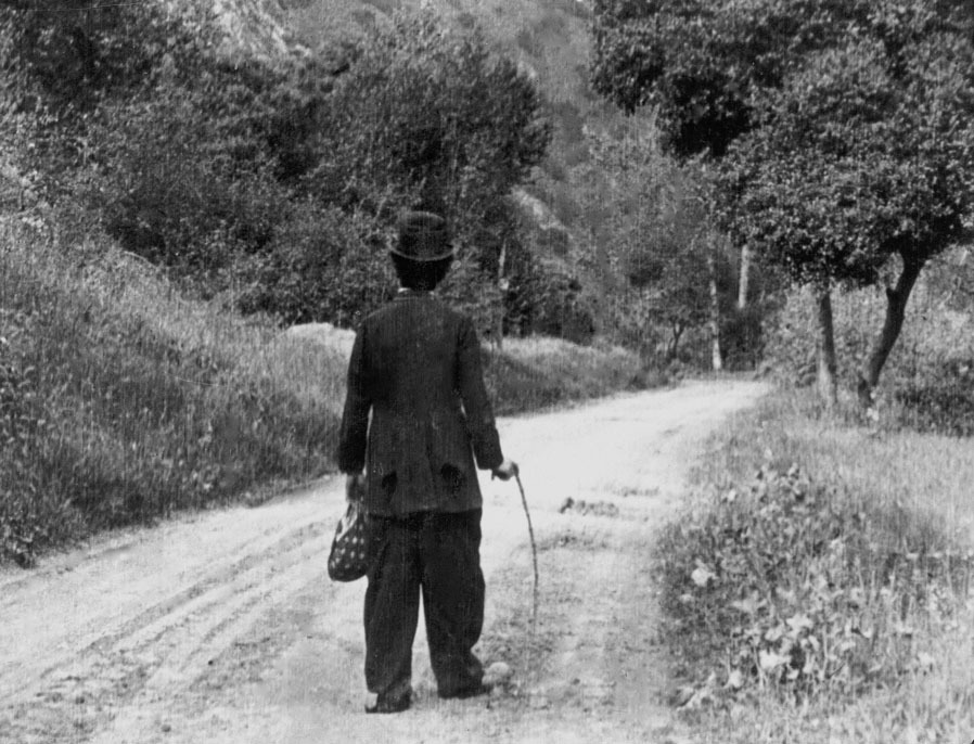 Photographie de Charlie Chaplin, de dos, dans Le vagabond (The Tramp), 1916.